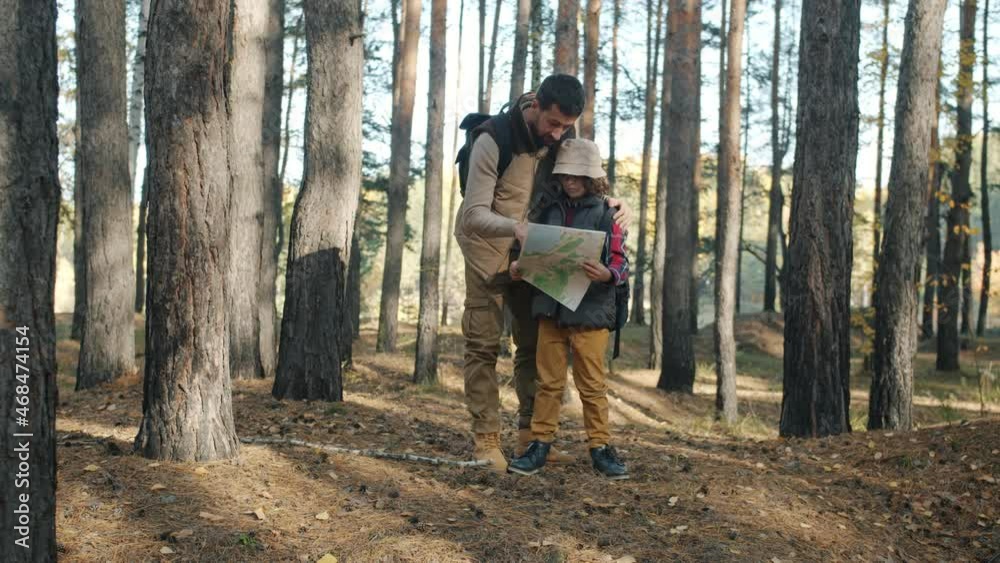 Father and son tourists are looking at map and talking standing in beautiful forest together on autumn day. Tourism and family concept. Father and son tourists are looking at map and talking standing in beautiful forest together on autumn day. Tourism and family concept.