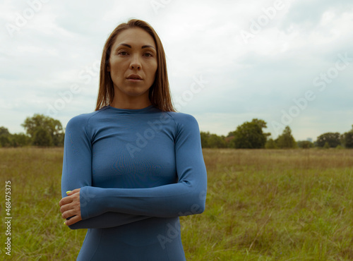 Portrait of a young sporty brunette girl in a blue sweater on the field. Exercise in nature