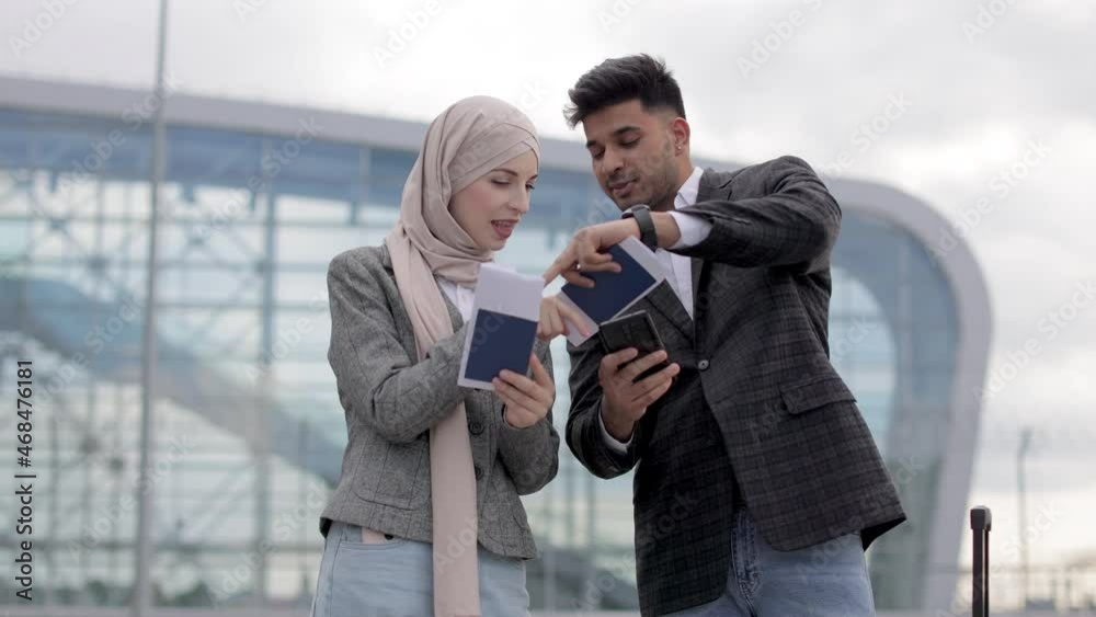 Positive Arab couple in jackets and jeans, standing outside airport ...