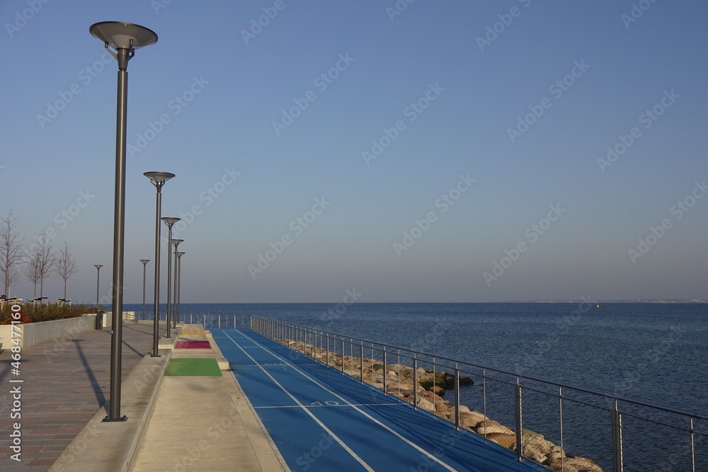 Jogging running lanes with white lines, blue artificial textured ground. Lampposts and handrails by the sides. Natural landscape and sea view on a sunny day. Reidi tee promenade, Tallinn, Estonia