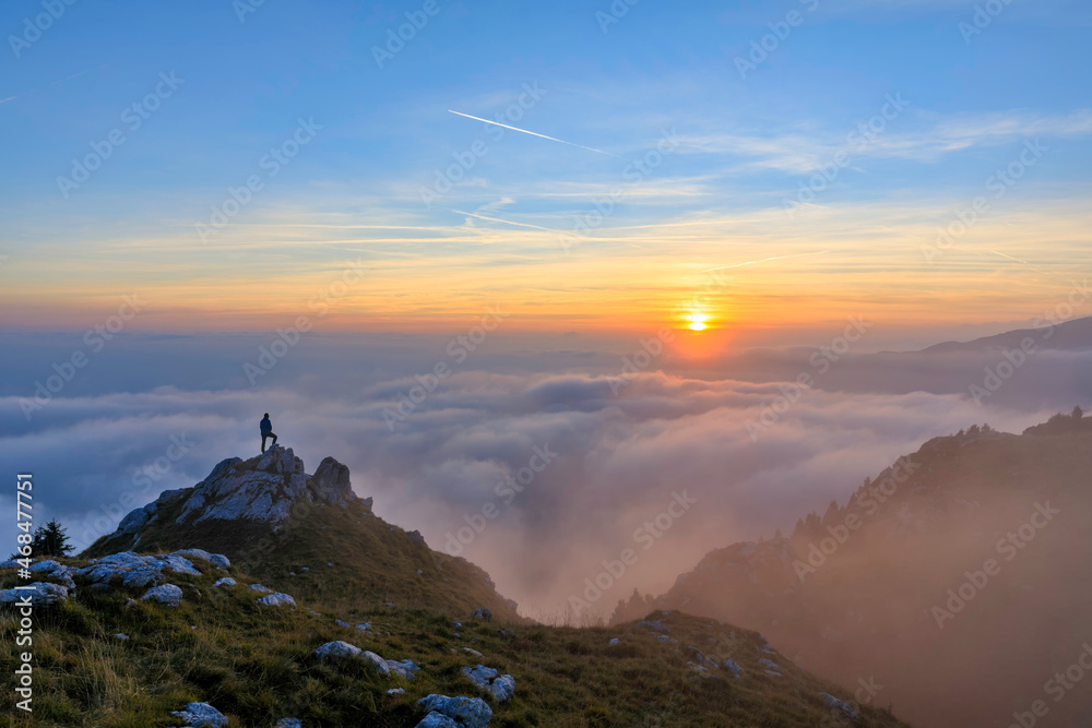 Escursionista sopra la montagna ammira un mare di nuvole al tramonto.