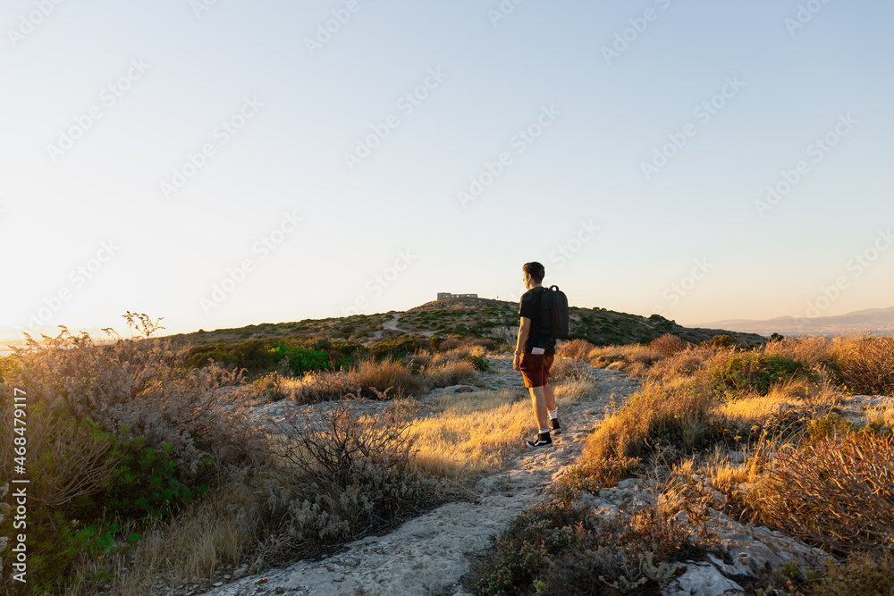 Panoramic back view of a backpacker looking over the horizon on the hills of Calamosca at sunset