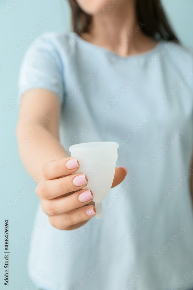 Woman holding menstrual cup on blue background, closeup Woman holding menstrual cup on blue background, closeup
