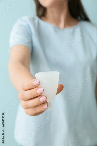 Woman holding menstrual cup on blue background, closeup