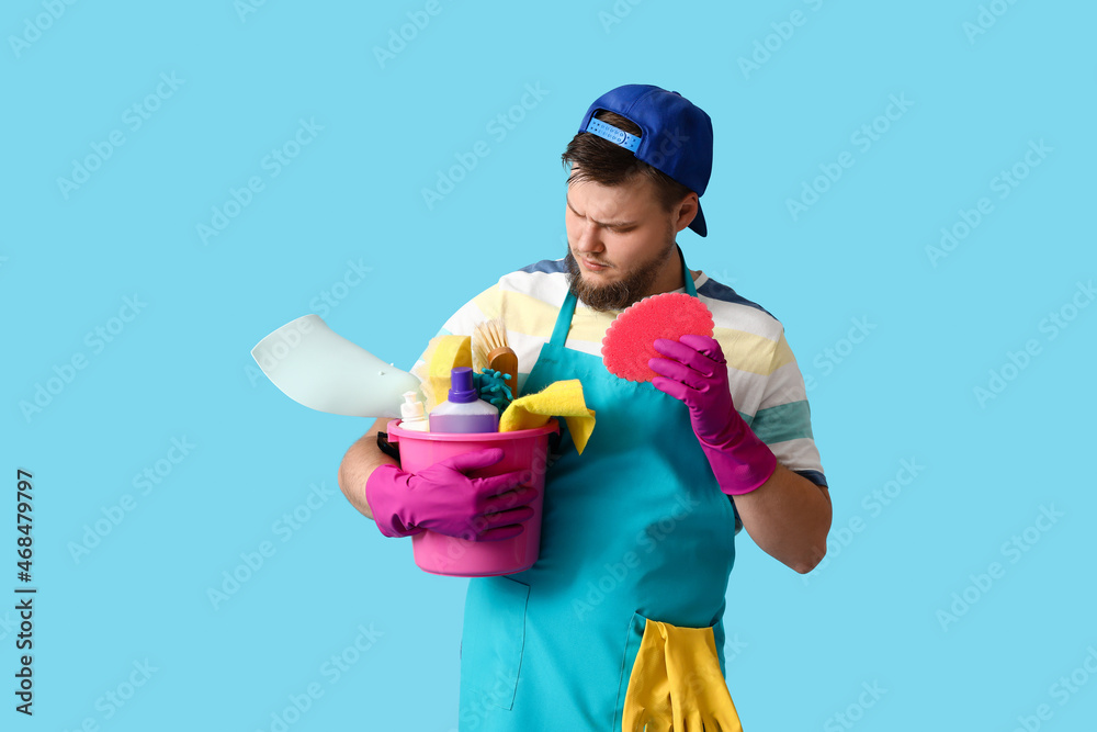 Young man with cleaning supplies on blue background Young man with cleaning supplies on blue background