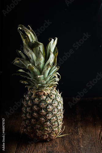 Ripe Tropical Pineapple on a wooden table with dark background. Tropical fresh healthy fruits. Dramatic lighting.