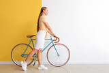 Pretty teenage girl with bicycle near color wall