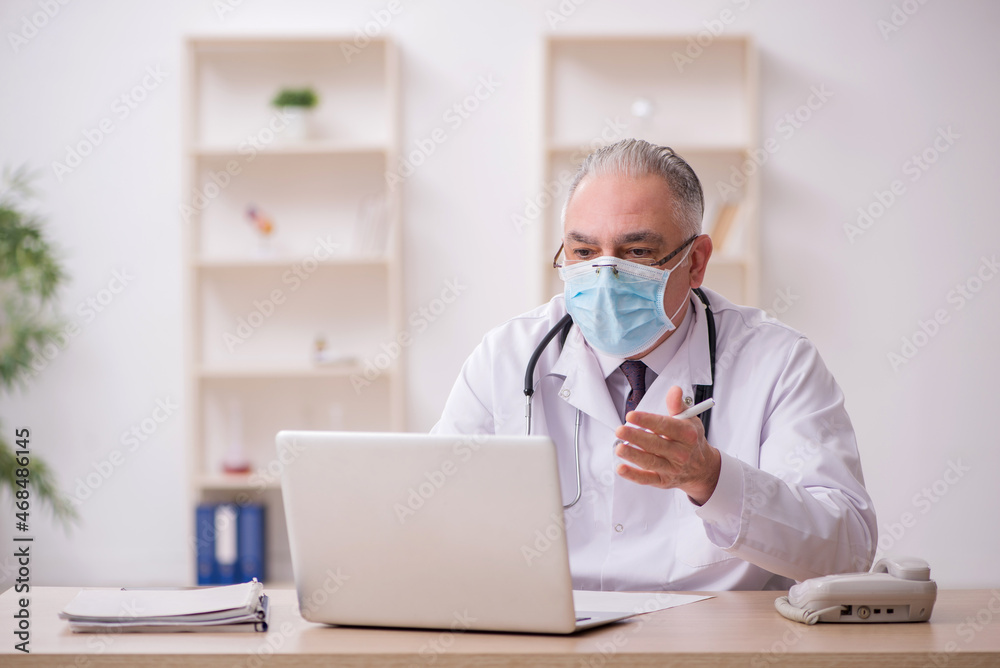 Old male doctor working in the clinic during pandemic Old male doctor working in the clinic during pandemic