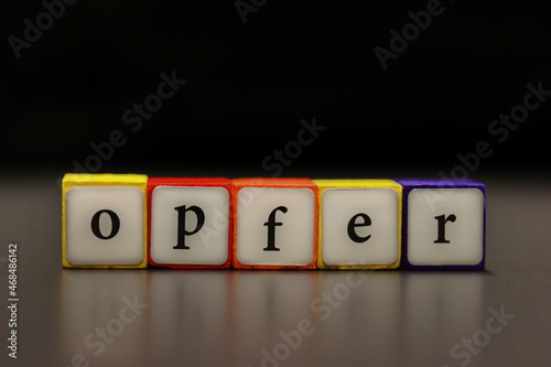 The word VICTIM (German: OPFER) written on colorful wooden cubes isolated on a black background