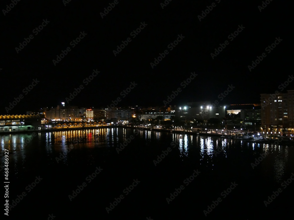 Medium wide shot of the seaport of Puerto Rico at night, with colorful lights reflected in the waters