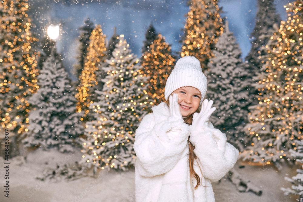 Obraz premium cute caucasian blonde girl in white eco fur coat, hat and gloves walking in the winter christmas forest. New year, fairy tale, fashion concept