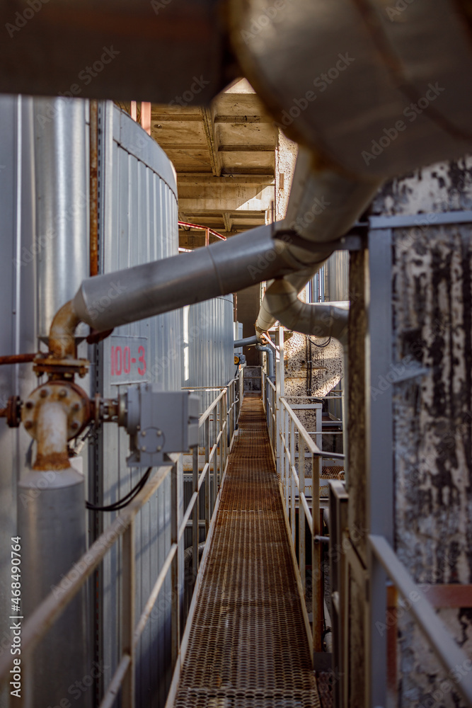 Section of manufacturing plant with pipes and metal bridge between industrial storage containers Section of manufacturing plant with pipes and metal bridge between industrial storage containers