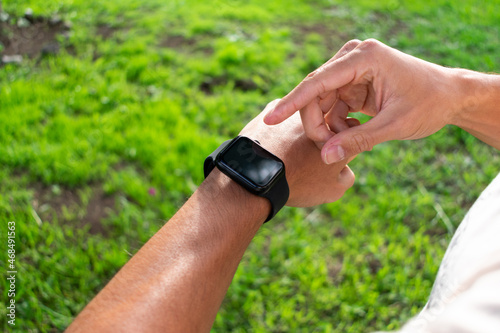 Close up of the wrist of a young latin man with a black rectangular smartwatch in the park. Technology, black screen.
