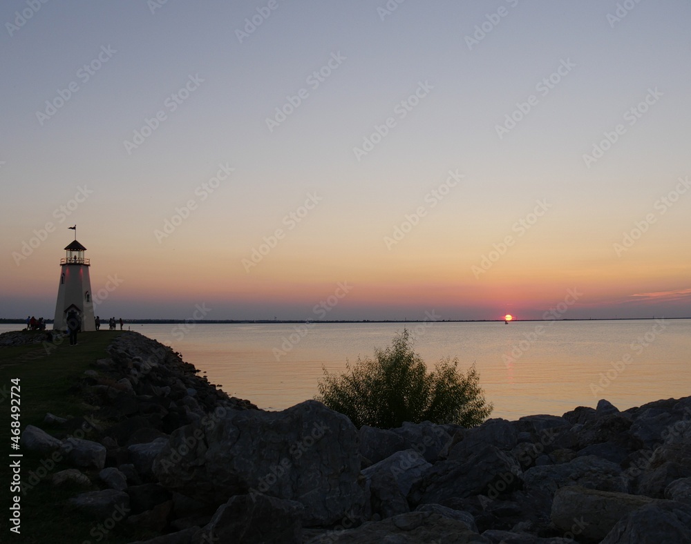 Lighthouse view with a sunset reflected in the lake, with silhouttes of people