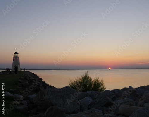 Lighthouse view with a sunset reflected in the lake, with silhouttes of people