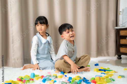 Children playing colorful wooden blocks in home,Sitting on floor,Boy unhappy.