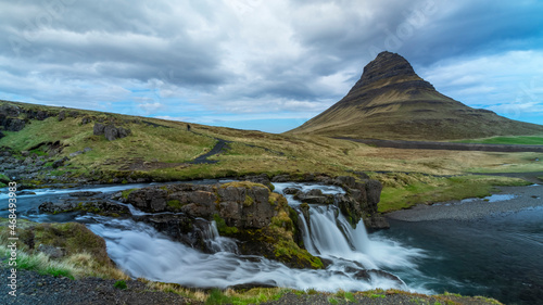 Low angle view of the Kirkjufellsfoss water fall near Grundarfjordur town in Iceland with famous Kirkjufell mountain in the background.