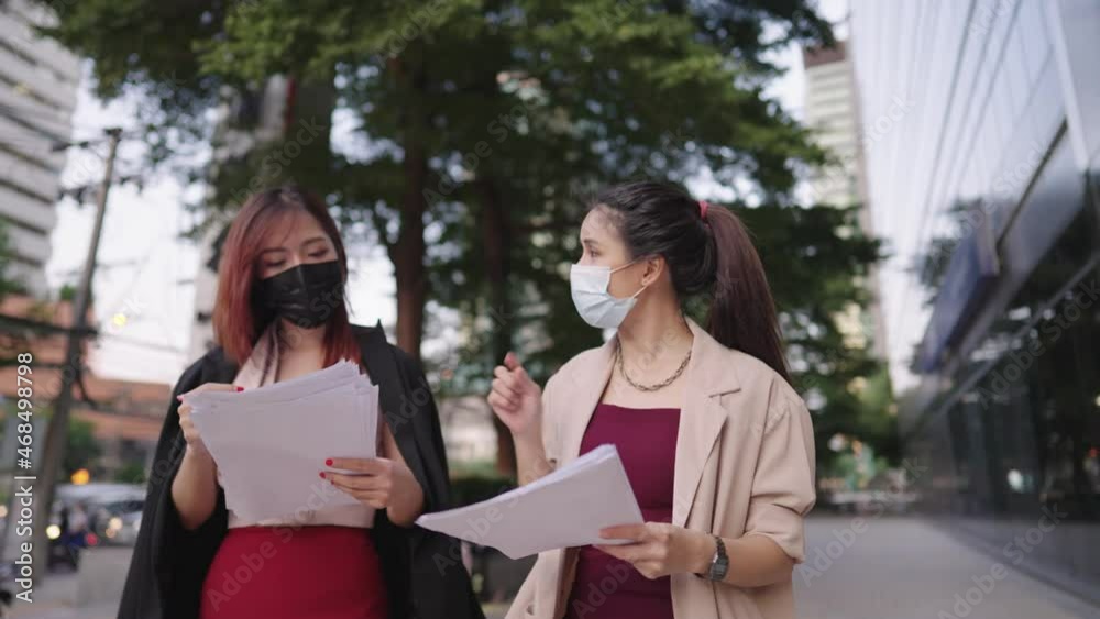 Two hard working asian office workers wear surgical mask holding work paper walking and discuss project briefing, work pressure and stress, solving problem on working site, meeting preparation paper Two hard working asian office workers wear surgical mask holding work paper walking and discuss project briefing, work pressure and stress, solving problem on working site, meeting preparation paper
