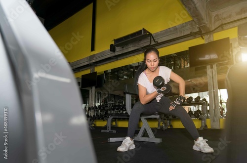 Young asian women training do muscle building exercises using dumbbells.Young fitness woman taking a dumbbell from rack in gym.Fitness dumbbells, weights equipment,Gym sport fitness concept.