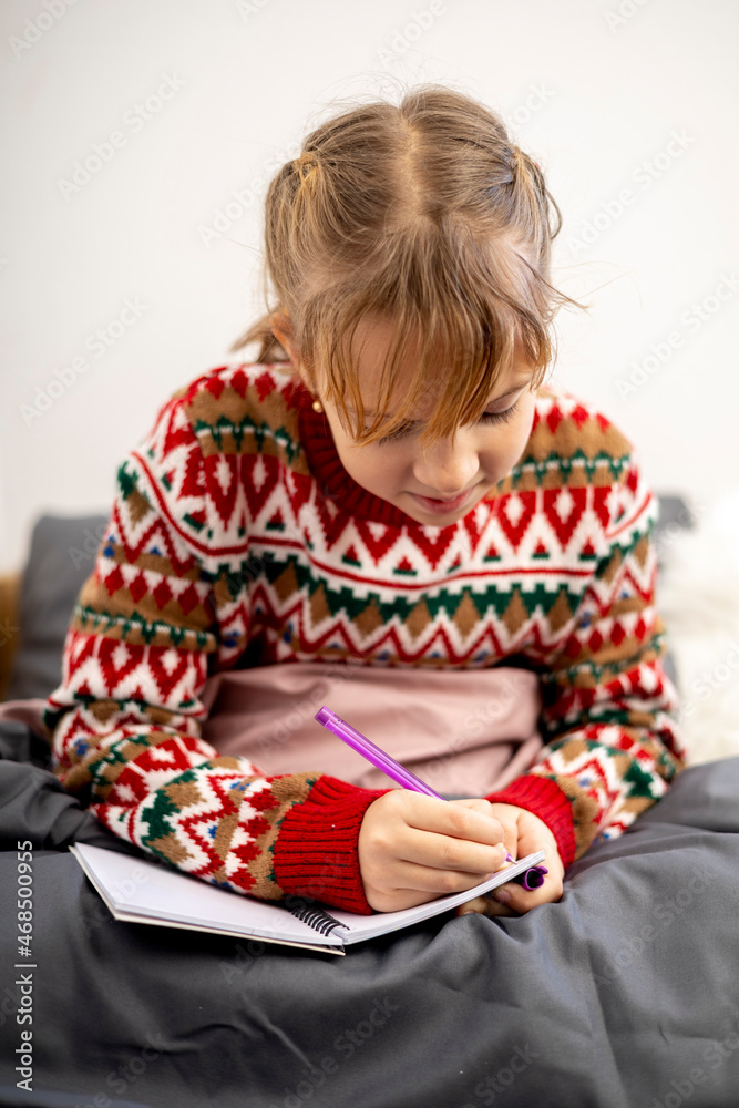 Girl makes a wish leaf. Child in Christmas pajamas sits on the bed.