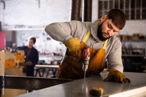 Portrait of confident man mechanic drilling metal sheet in workshop
