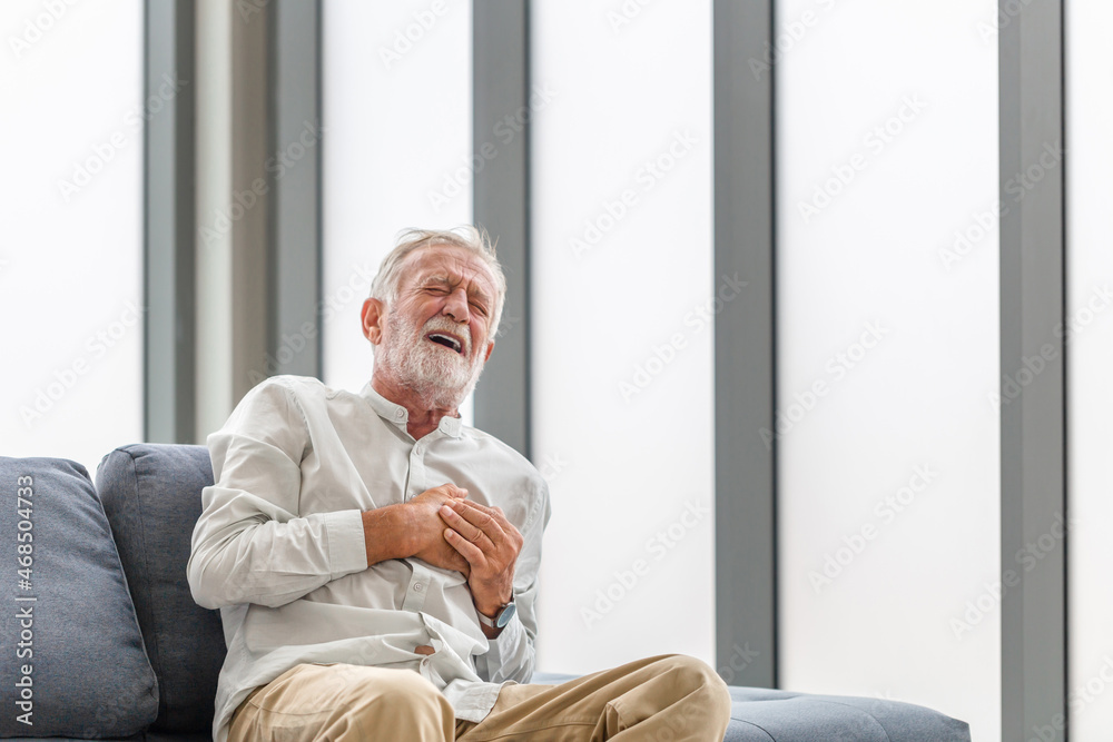 Mature man presses hand to chest has heart attack suffers from unbearable pain, Senior man with pain on heart in living room Mature man presses hand to chest has heart attack suffers from unbearable pain, Senior man with pain on heart in living room