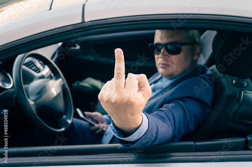 Rude and furious driver giving middle finger to car. A businessman in an expensive car shows an indecent gesture through the car window. Parliamentary immunity, concept disregard for law photo