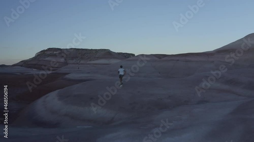 Drone footage of man jogging through smooth rocky desert mounds in Mars State Park, Utah, USA during cold blue hour sunset with a clear sky photo