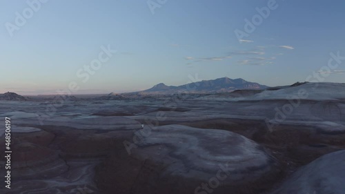 Drone footage of man walking through cold desolate alien like mound landscape during blue hour sunset in Mars States Park in Utah, USA with Mt. Ellen Peak in the far background photo