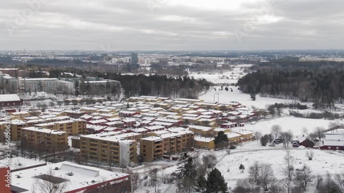 Akalla Stockholm, Sweden. Drone Footage Flying Through Small Swedish European Snow Covered Winterscape District Town With Red Yellow Apartment Buildings And Trees In The Background And A Cloudy Sky. photo