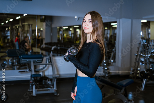Sportive woman doing warm-up in gym with dumbbells in hand. Woman in gym doing abdominal exercises in the fitness club. In sportswear. Slimming and healthy lifestyle concept