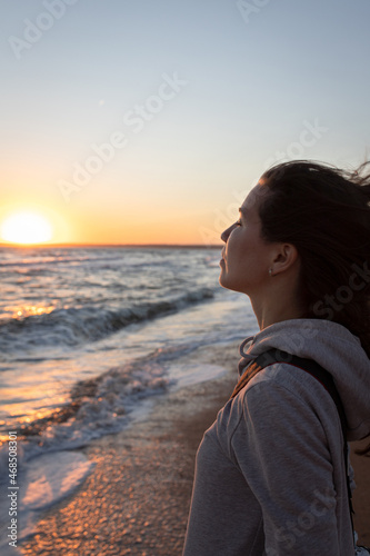 A woman enjoys the view of the sea at sunrise. Side view.