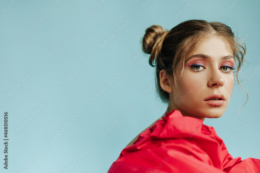Close-up fair-skinned young woman stares piercingly into camera against backdrop with space for text. Girl with bright makeup and blond hair in red outfit. Leisure lifestyle and beauty concept. Close-up fair-skinned young woman stares piercingly into camera against backdrop with space for text. Girl with bright makeup and blond hair in red outfit. Leisure lifestyle and beauty concept.