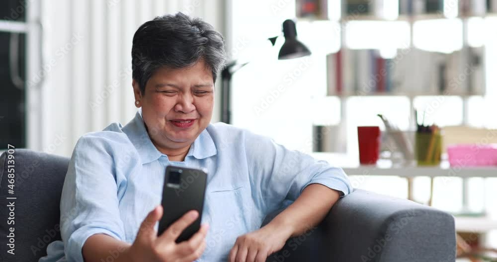 Middle aged Asian female relaxing on couch and talking on mobile phone in sunlit living room on weekend at home Middle aged Asian female relaxing on couch and talking on mobile phone in sunlit living room on weekend at home