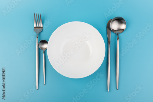 Empty plate with fork and spoon on blue background. Flat lay Dishes for breakfast, lunch or dinner Mock up