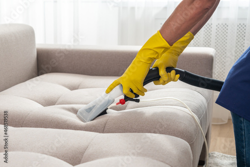 Close-up of housekeeper holding modern washing vacuum cleaner and cleaning dirty sofa with stain with professionally detergent. Professional springclean at home concept photo