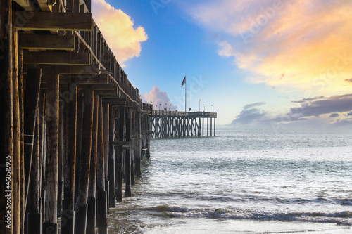 a stunning shot of a long winding brown wooden pier at the beach with vast blue ocean water and silky brown sand with blue sky and powerful clouds at Ventura Pier in Ventura California USA photo