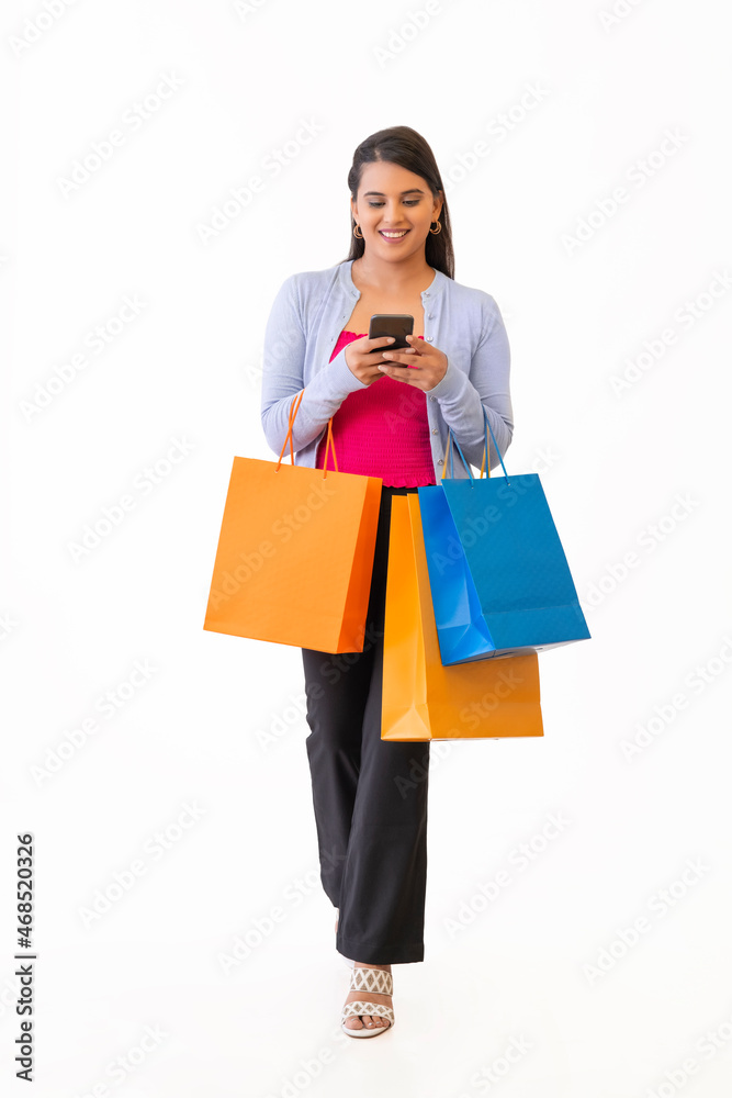 Beautiful young lady with shopping bags and holding mobile in her hand Beautiful young lady with shopping bags and holding mobile in her hand