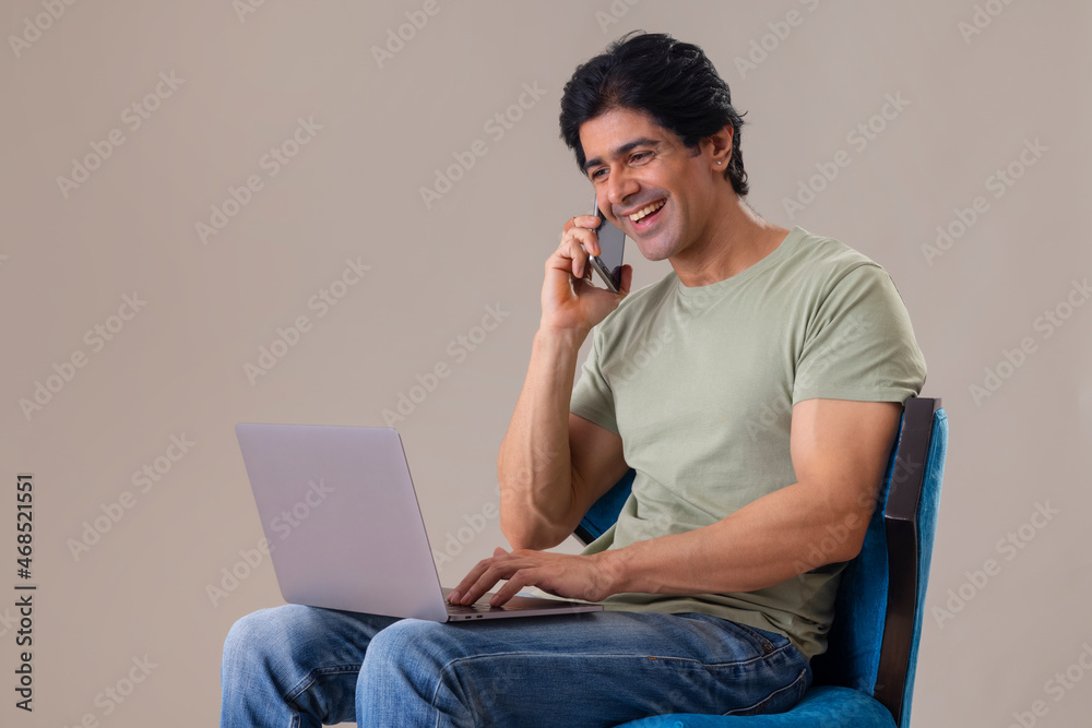 Indian middle age man talking on cell phone and working on laptop Indian middle age man talking on cell phone and working on laptop