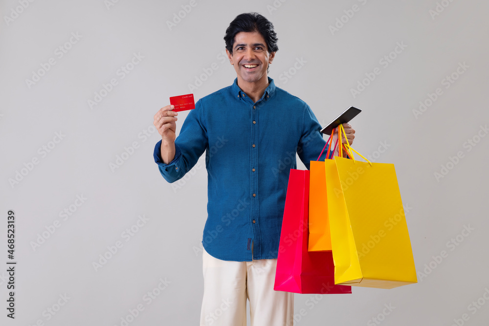 Indian man standing in front of camera with holding a credit card, tablet and shopping bags Indian man standing in front of camera with holding a credit card, tablet and shopping bags