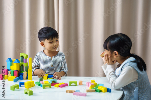 Children play with colorful toy blocks. Little boy and girl is building a tower of toy blocks sitting on a dark floor in a bright livingroom.