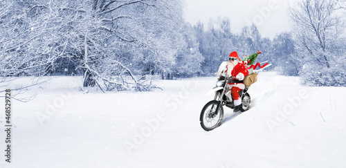 Santa riding a motorbike delivering Christmas or New Year presents, parcels on snow winter landscape background
