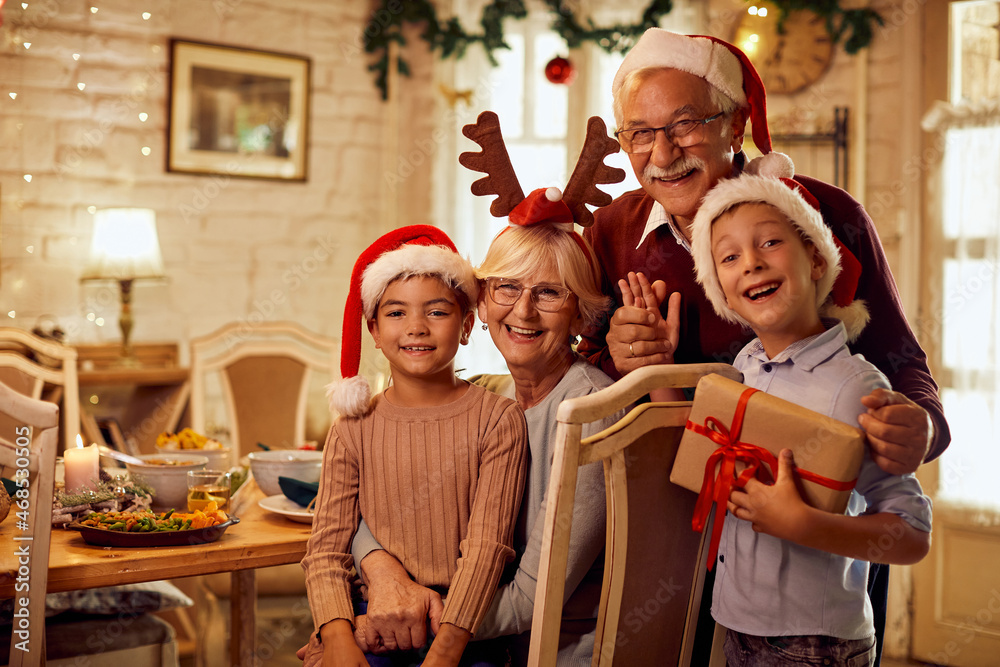 Happy grandparents with grandkids celebrate Christmas at home and look at camera. - obrazy, fototapety, plakaty 