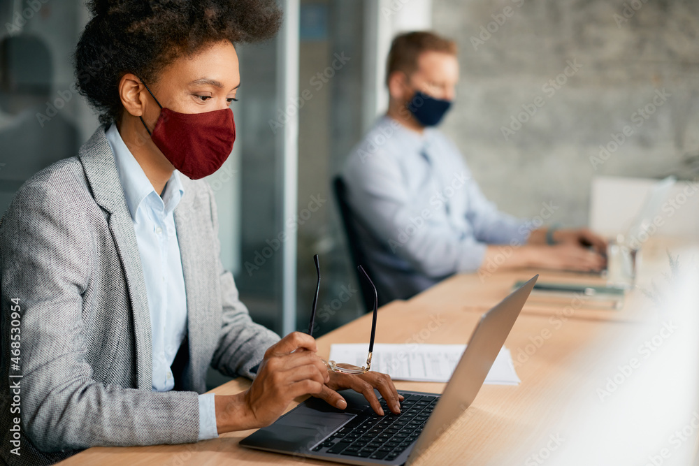 © Drazen - Black businesswoman wears face mask while working on laptop in office during coronavirus pandemic. © Drazen - Black businesswoman wears face mask while working on laptop in office during coronavirus pandemic.