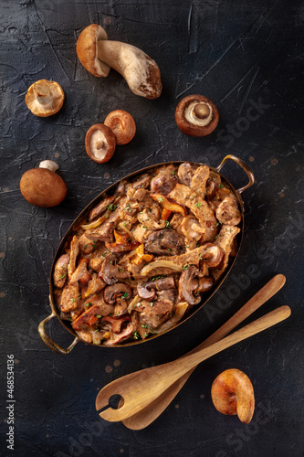 Beef stroganoff, mushroom and meat ragout with cream sauce, in a cooking pan with ingredients, overhead flat lay shot on a black background