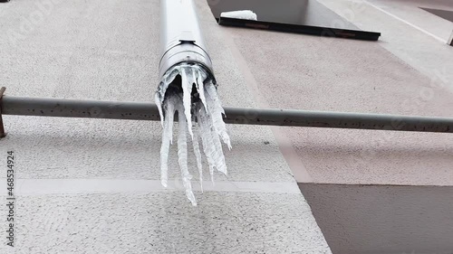 Frozen icicles hang in winter on a drainpipe on the wall of the house, outdoors