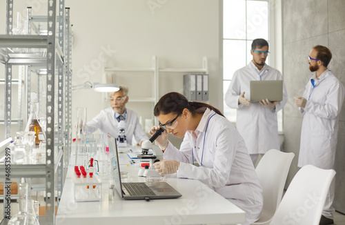 Clinic lab examination. Young smart woman examines test samples with a microscope in a modern medical laboratory. Concept of science  chemistry  technology  biology and people.