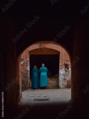 Street scene in Marrakech of two woman dressed with blue typical moroccan outfit in a food shop © Elisenda