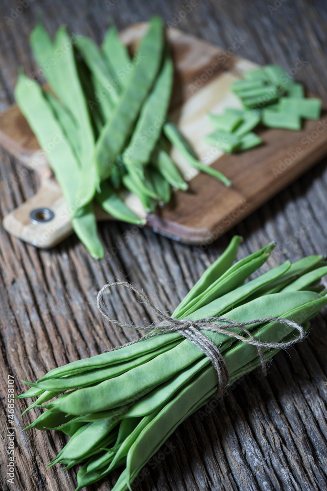flat green beans tied with string on an old wooden plank in the foreground in focus. wooden plank with cut vegetables in the background. selective focus. copy space, text space. vertical photography. flat green beans tied with string on an old wooden plank in the foreground in focus. wooden plank with cut vegetables in the background. selective focus. copy space, text space. vertical photography.