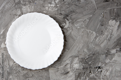 Empty white plate over gray concrete background. top view